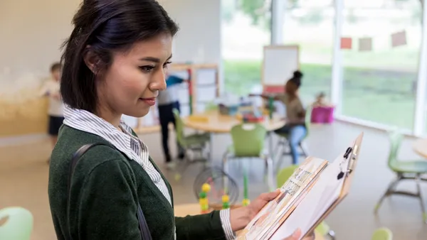 As young students interact in the background, a woman teacher reviews her lesson plans for the day.