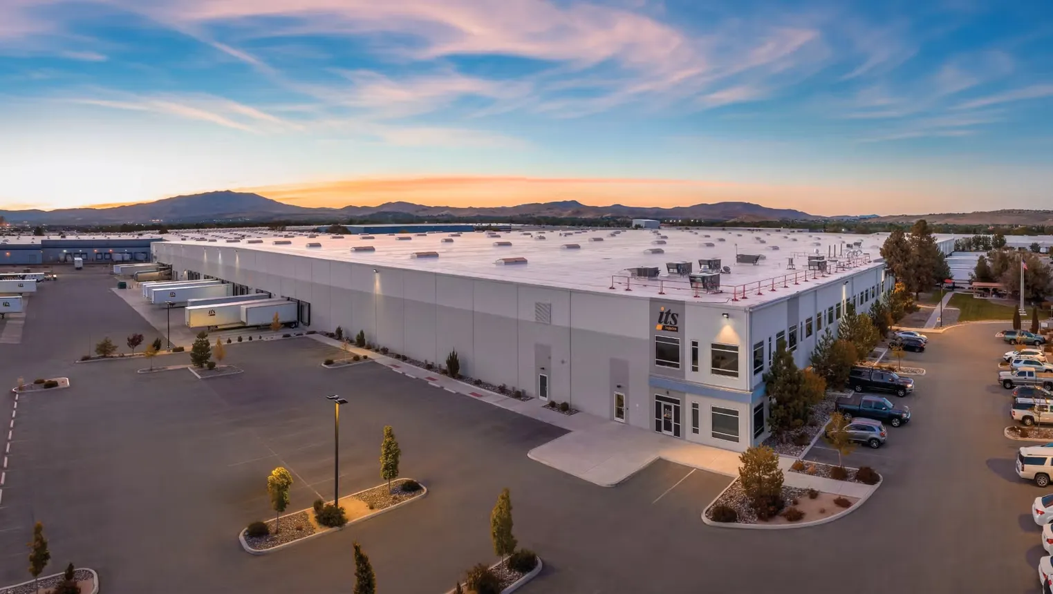 A look outside a distribution center at night time with a view of the parking lot and trucks at the dock doors.