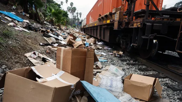 A freight train on tracks strewn with cardboard boxes and other litter.