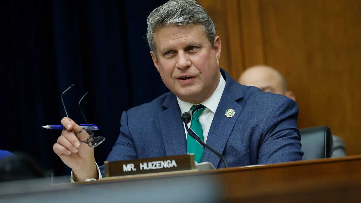 Rep. Bill Huizenga speaks with glasses and a pen in one hand.