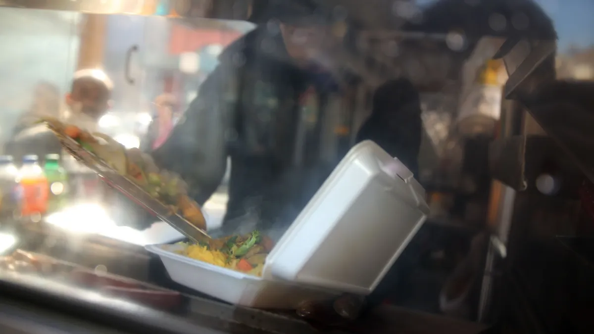 A cook ladles food into a styrofoam takeout container in New York