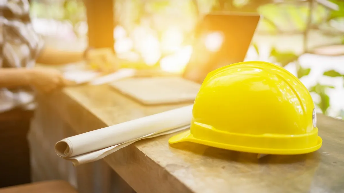 A creative image of a hardhat next to rolled up plans.