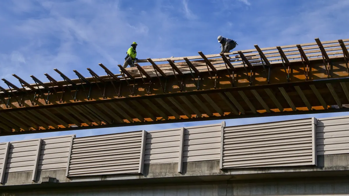 Two construction worker hgh up on a pedestrian bridge.