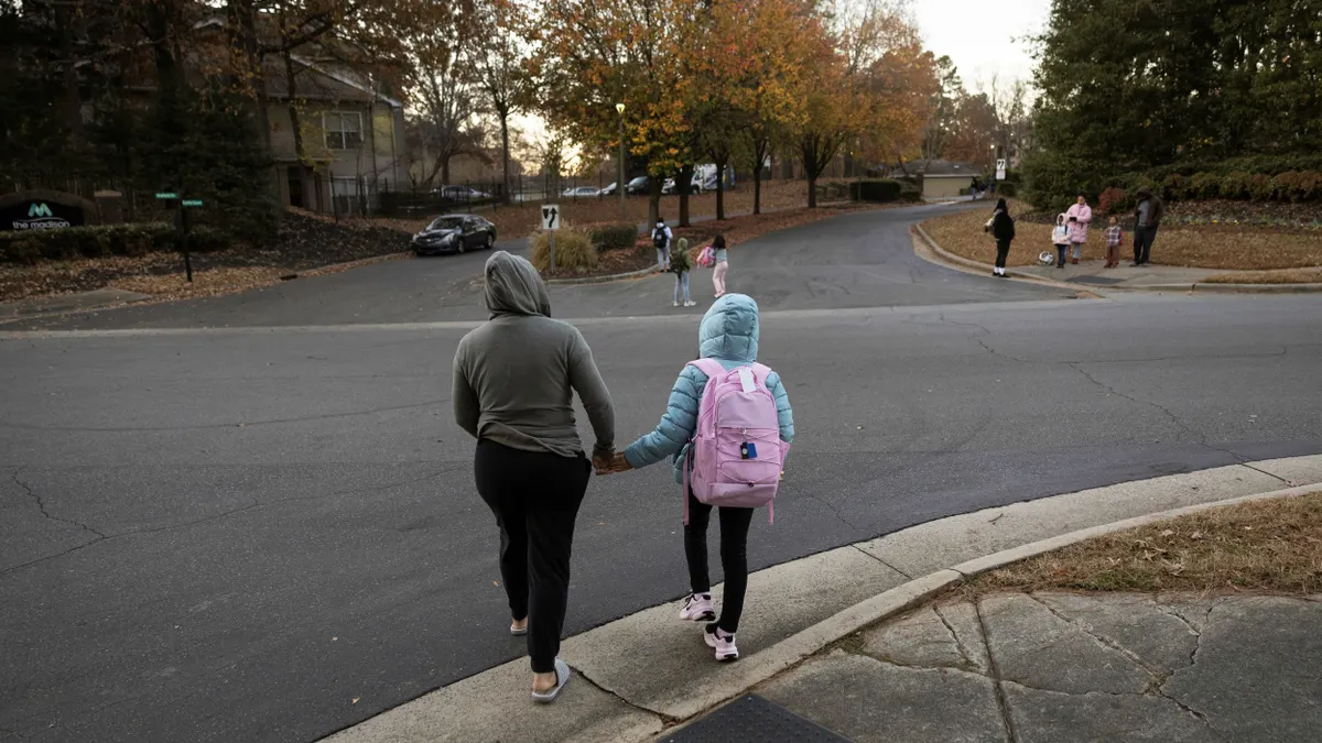 A parent crosses the street while holding her child's hand.