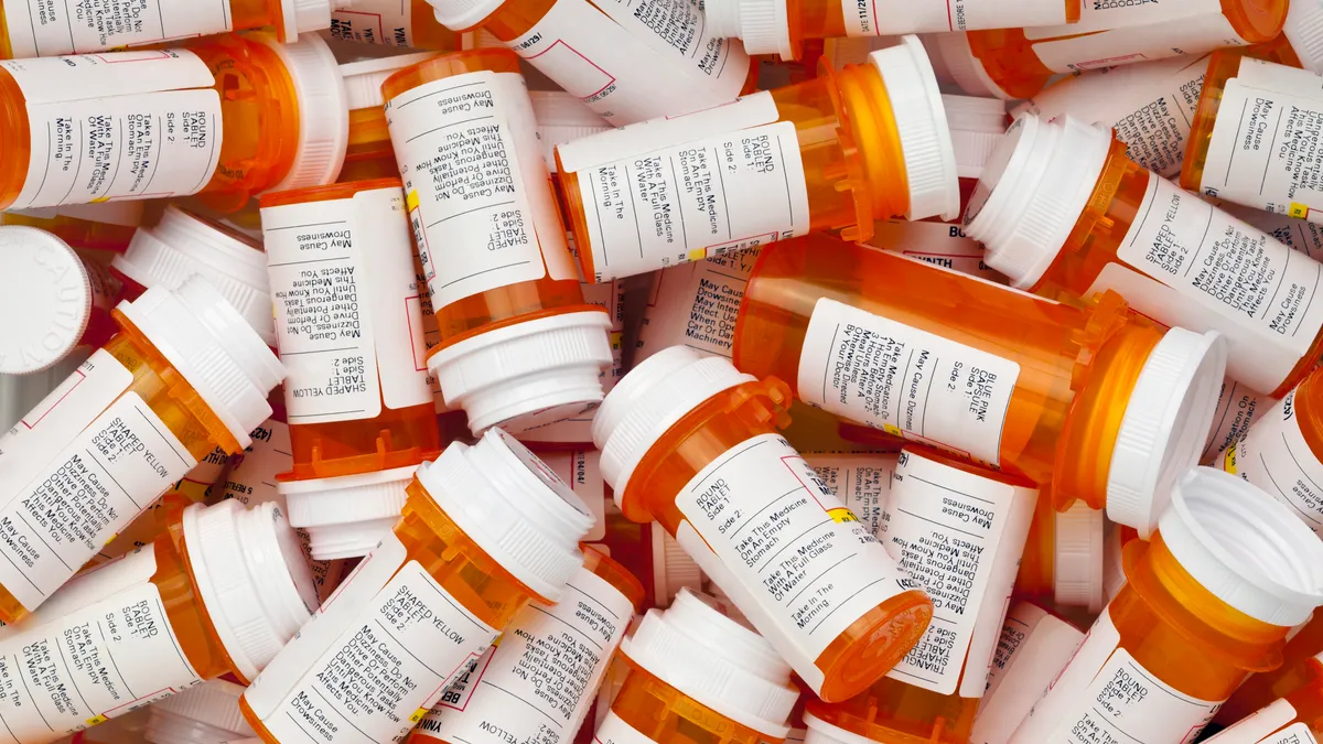 Dozens of orange prescription bottles with white caps and labels layered in a jumple.