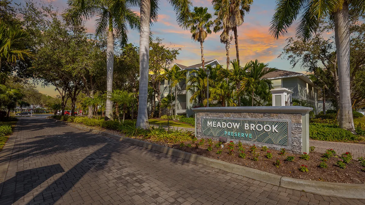 Apartment property with a sign and trees in the foreground.