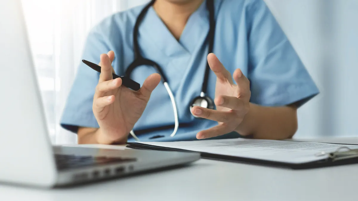 A doctor with a stethoscope sits in front of a laptop