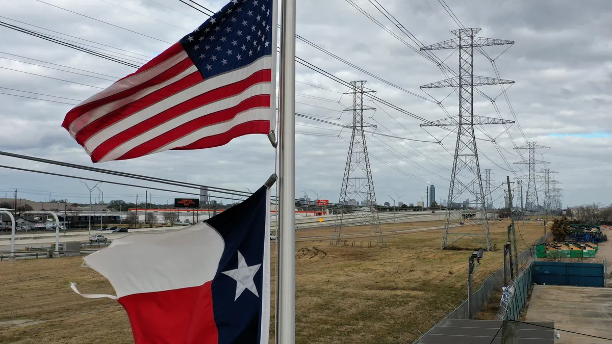 he U.S. and Texas flags fly in front of high voltage transmission towers