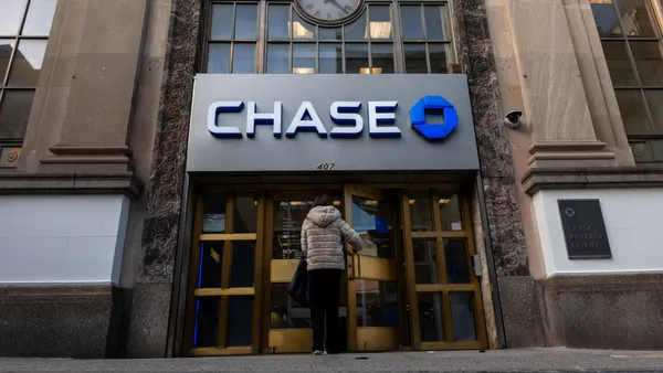 A person is shown from behind opening the metal and glass doors of a Chase bank branch, with the company's signage and logo above the doors.