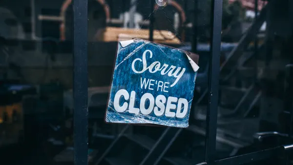 An image of a worn sign on a window that says "sorry we're closed."
