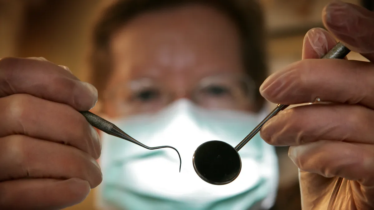 Patient's view of dentist holding two dental instruments.