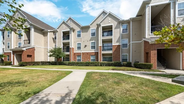 Three-story brick and tan apartment building with grass in the foreground