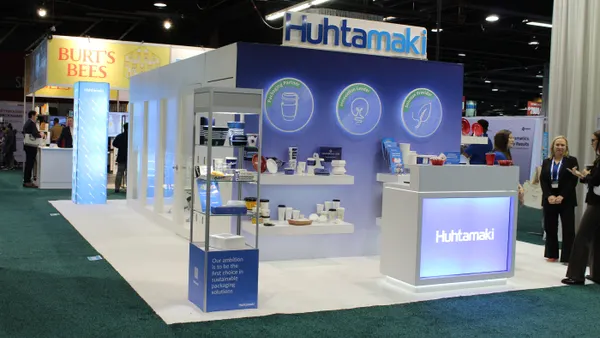 A booth at a trade show with Huhtamaki's blue branding and food service products on display.