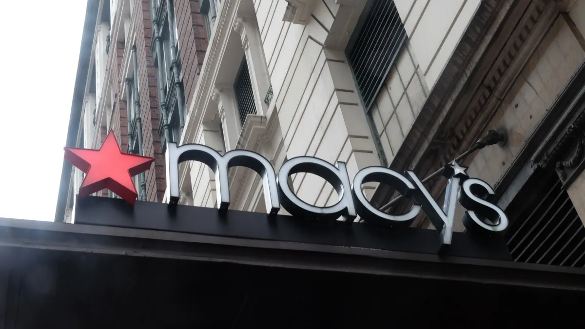 A closeup of a Macy's sign with a signature red star sits atop a store entrance overhang.