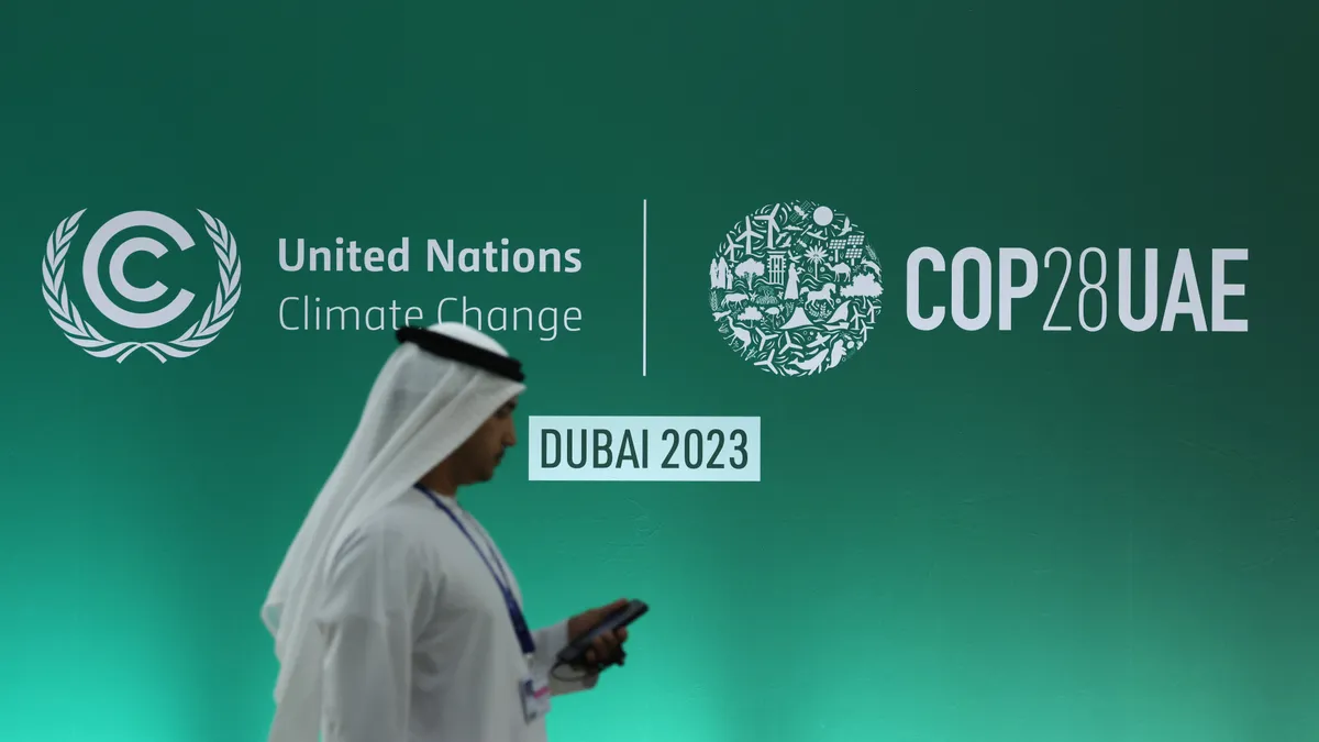 A person walks in front of a wall reading "United Nations Climate Change" and "COP28UAE."