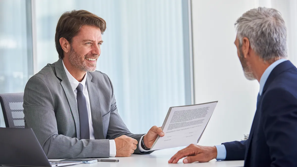 A lawyer holds out a document to show a client in an office