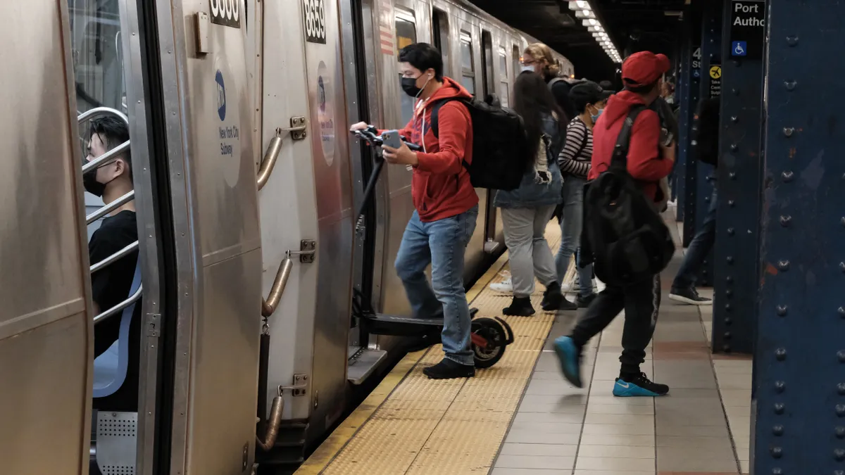 Several people wearing masks are entering and leaving a silver subway train at an underground station in New York City.