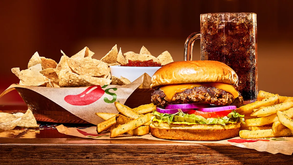 Chili's Big Smasher cheeseburger accompanied by sides of chips, fries and cola on a wooden dining table