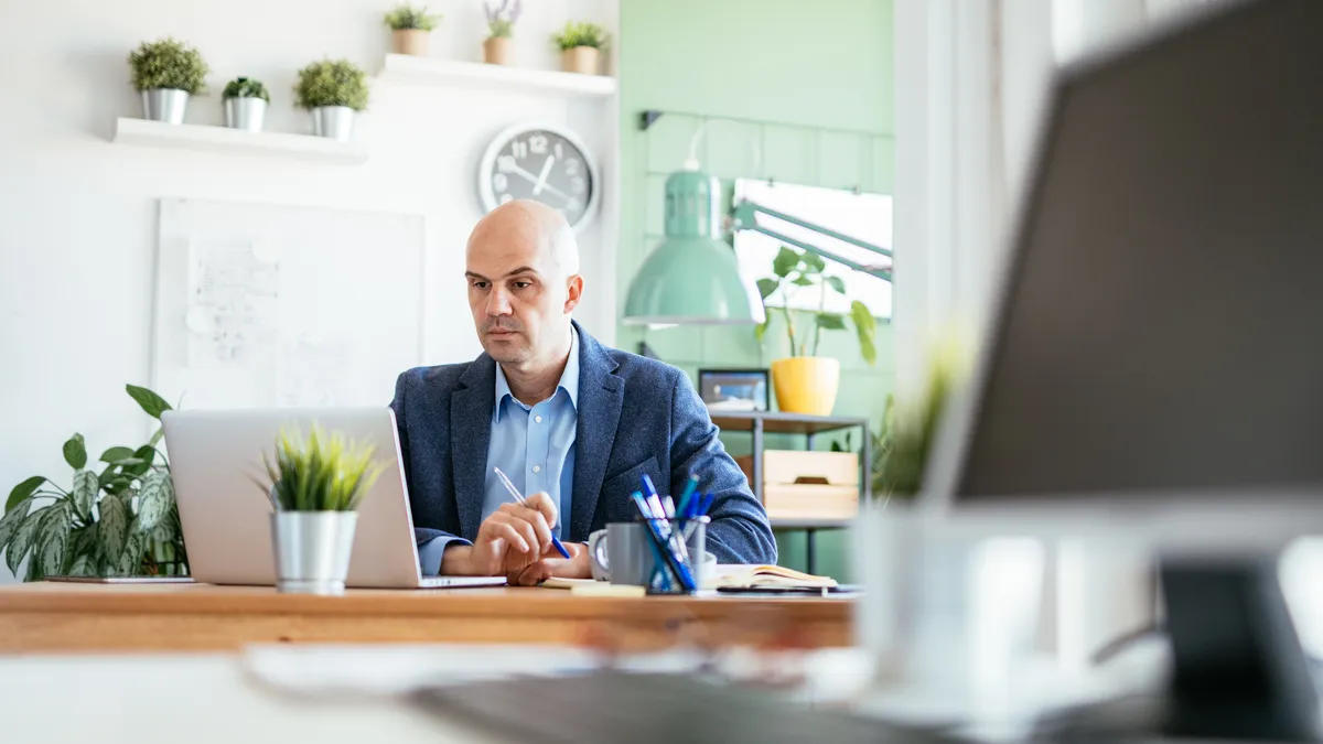 An employee is taking notes during a virtual meeting while working remotely from a home office.