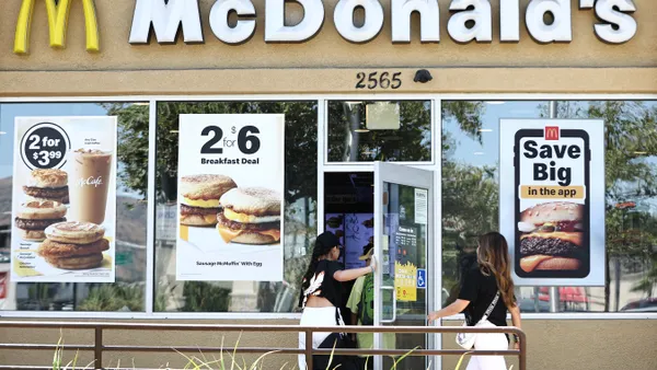 People enter a McDonald's restaurant that has posters on the windows advertising meal deals.