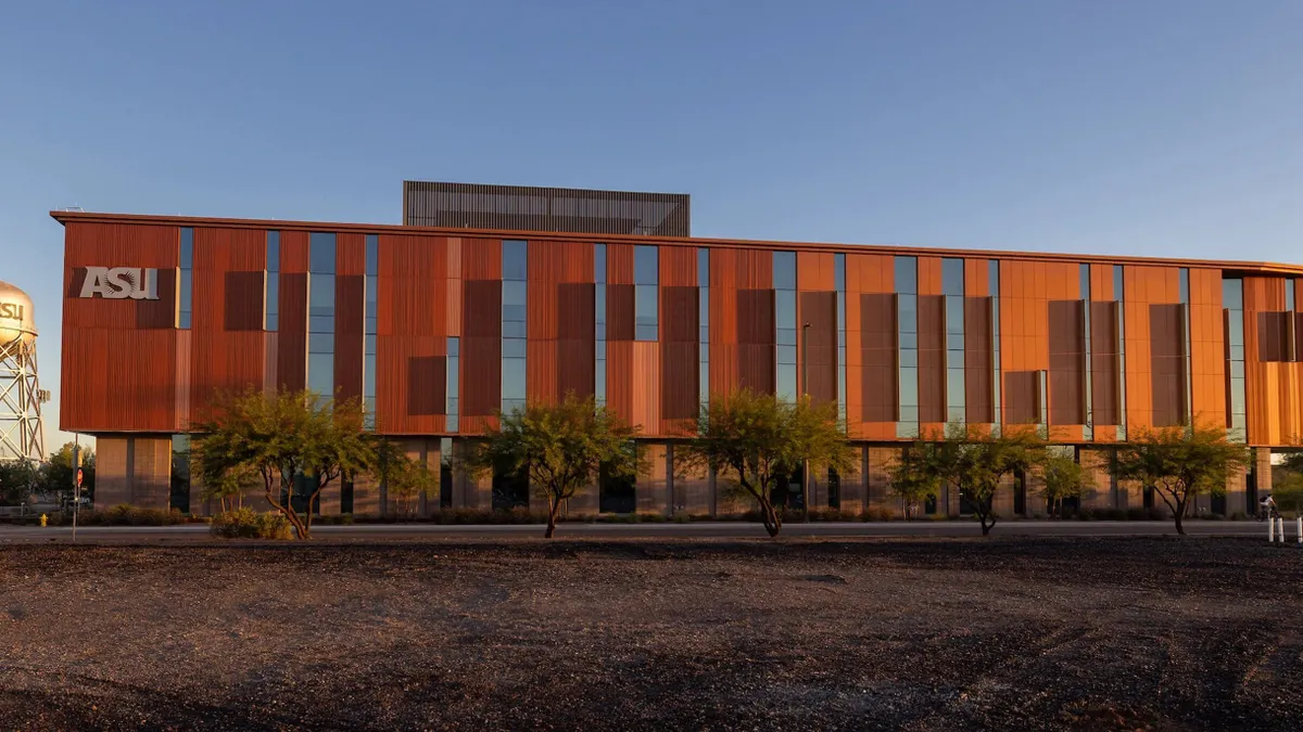 A building sits in the sunset in the background and occupies the central frame. It's a reddish color, with windows along the front.