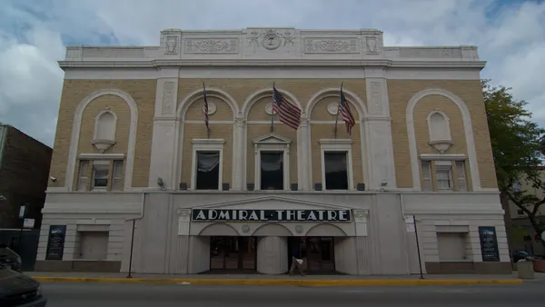 A view of a multistory theater made of stone and yellow bricks, with "Admiral Theatre" written on signage over the door.