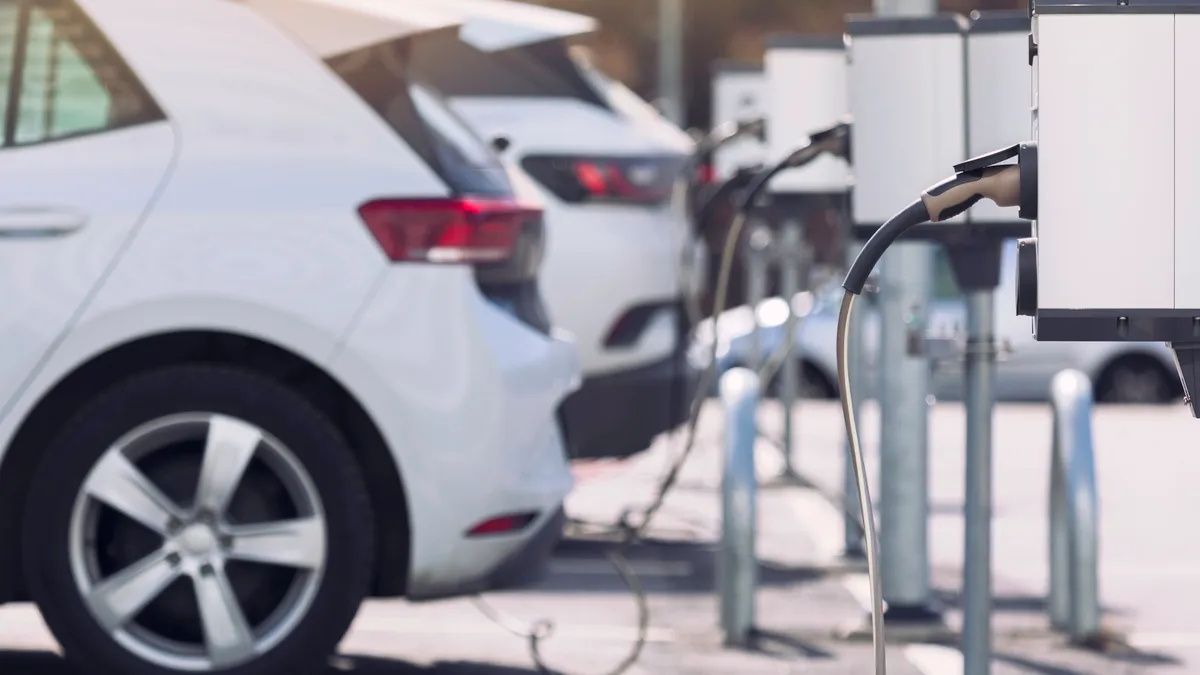 Several white cars are seen plugged into a line of electric vehicle chargers.