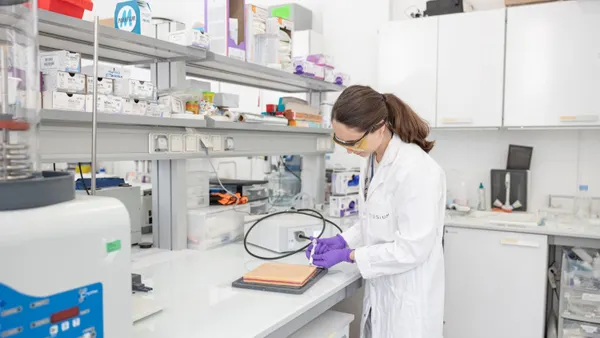 A Tissium employee in a white lab coat and purple gloves works with equipment in a laboratory.