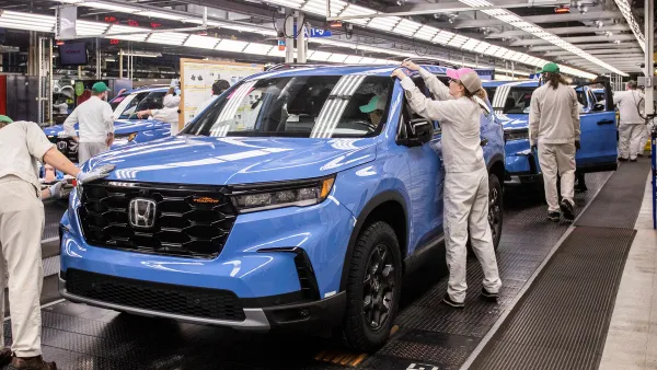 Workers in white uniforms perform an inspection of a blue 2023 Pilot TrailSport SUV on the assembly line at Honda’s Alabama Auto Plant.