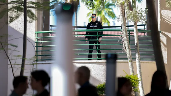 A person in a police uniform stands on a landing above people walking on the ground below who are not in focus.