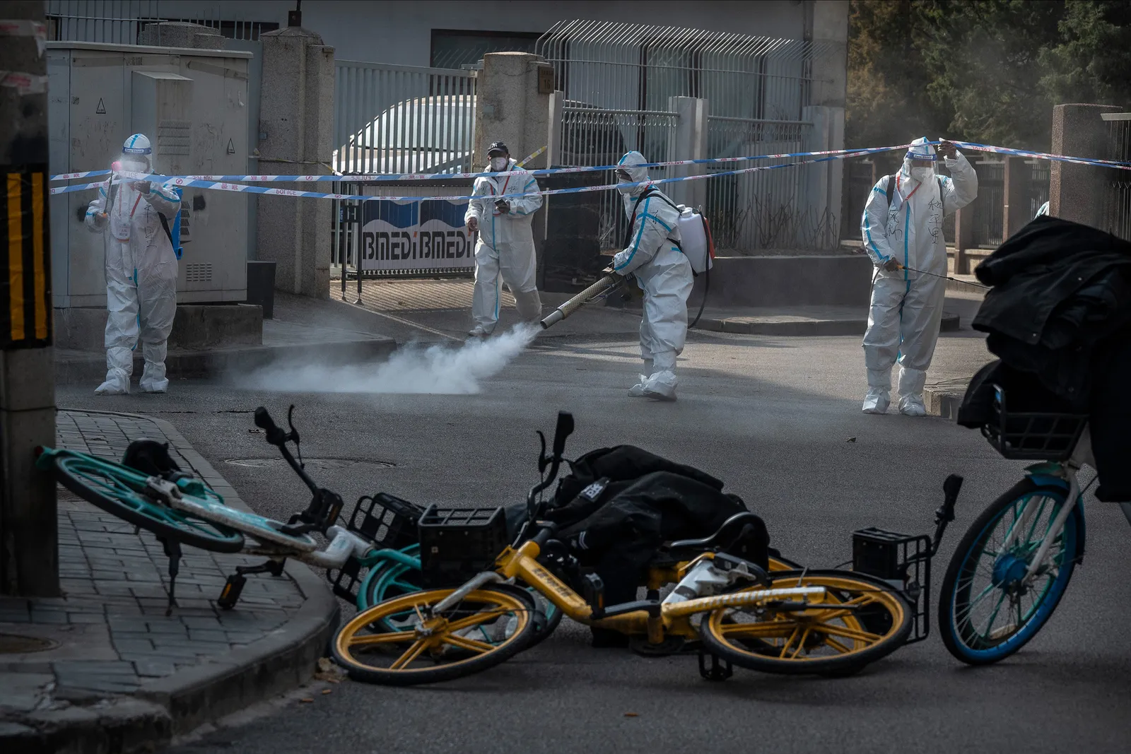 Several people wearing protective gear disinfect a street in a neighborhood.