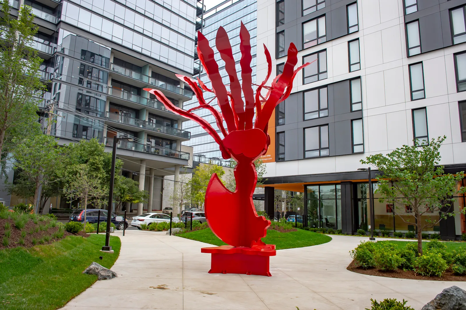 A courtyard with two buildings flanking a red sculpture of a hand.