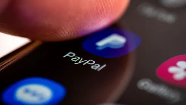 Close-up of an Android smartphone screen displaying the PayPal app icon and name, with a fingertip poised above the screen, indicating user interaction.