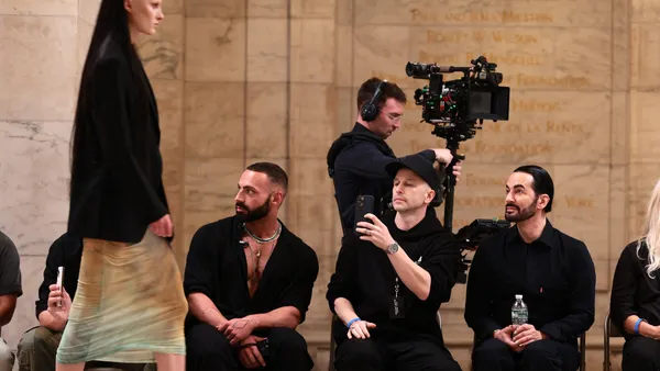 A model wearing Marc Jacobs walks while several people sit and watch in a row.