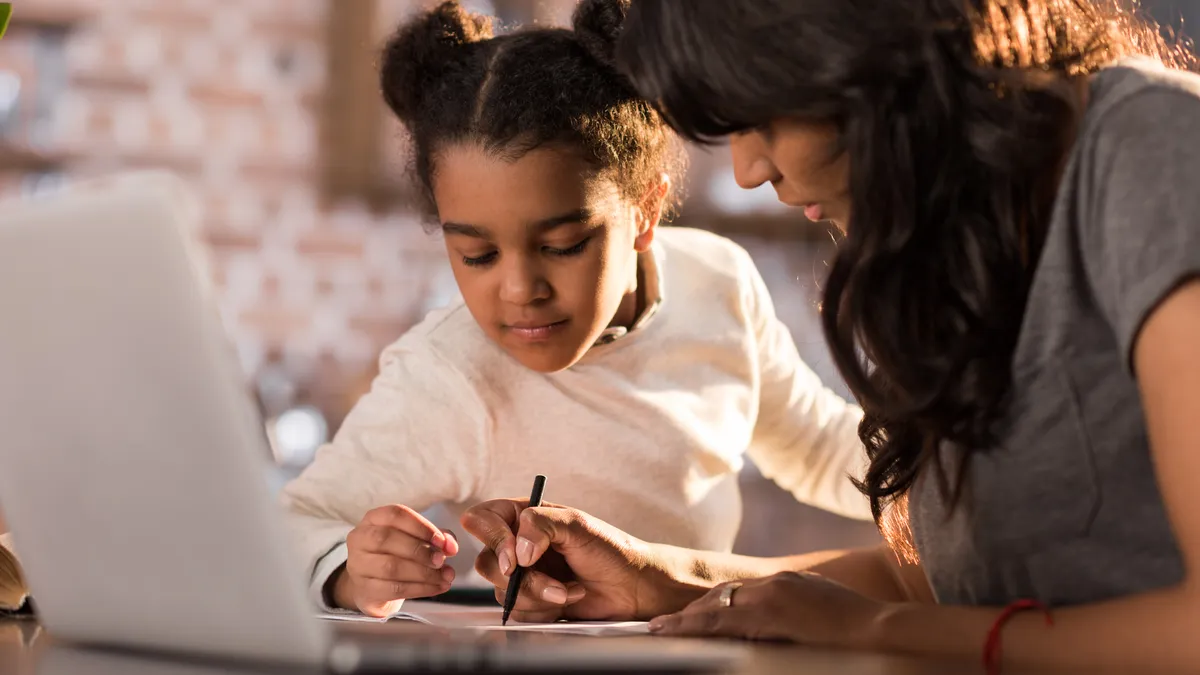 An adult and child sit next to each other at a table with a laptop on it