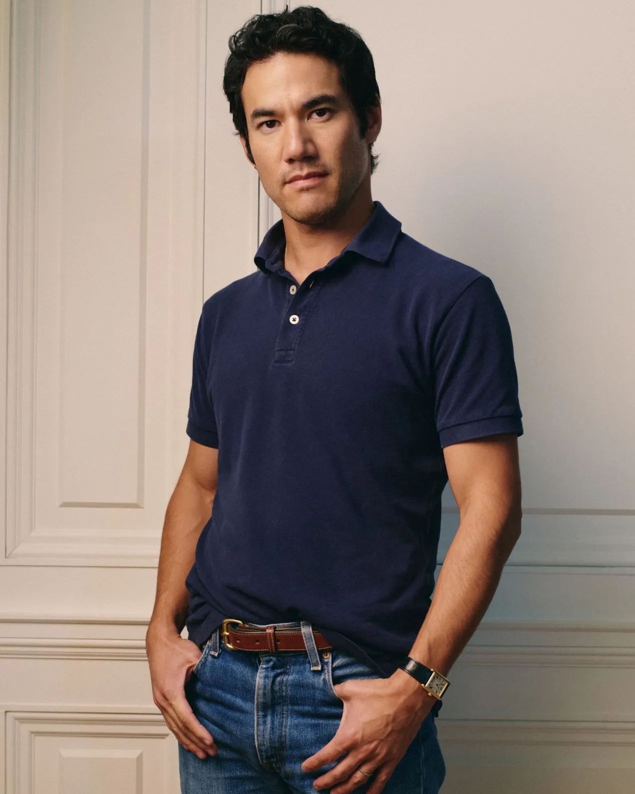 A person wears a dark blue polo shirt and stares at the camera.