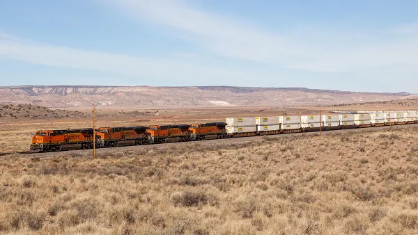 A rail train passes through a scenic route of dry land.