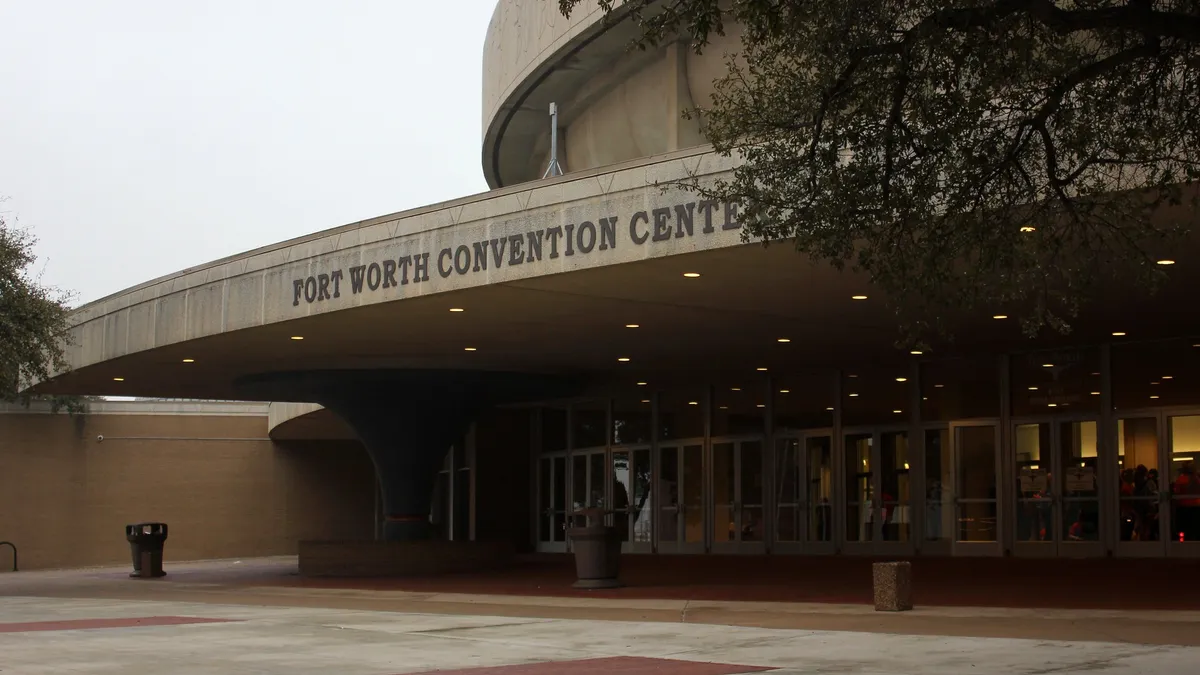 Curved entrance of the front of a beige building with many glass doors.