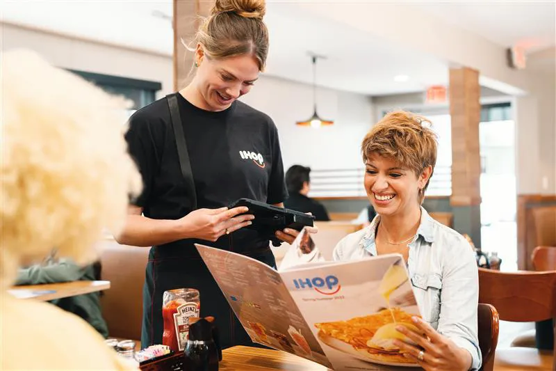 A picture of an IHOP server taking an order using a tablet.