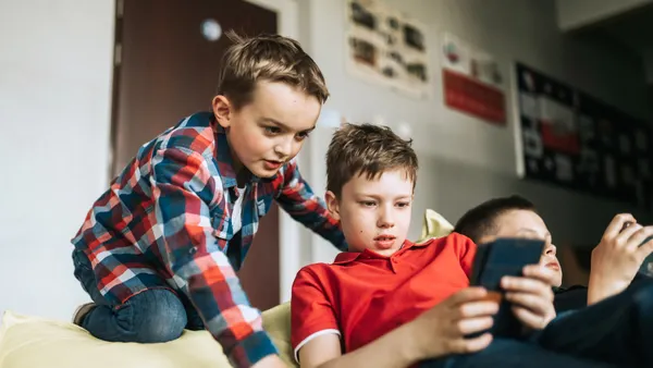 Three young boys relax on a bean bag and play on mobile phones in a school corridor.