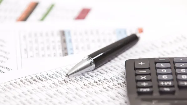 A photograph with a close up of a financial spreadsheet with a black caalculator on the right and a black pen in the middle.
