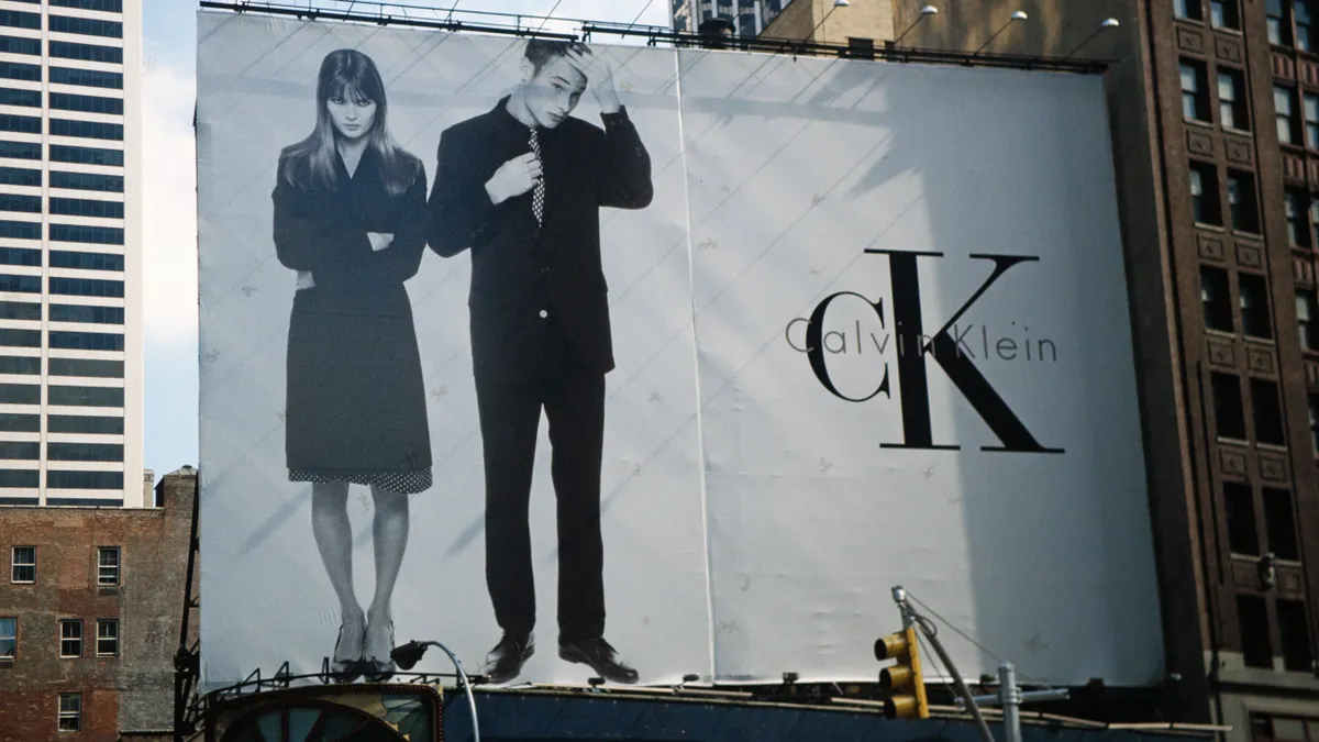 Surrounded by buildings, a black-and-white billboard features a couple standing on the left, with the Calvin Klein logo on the right.