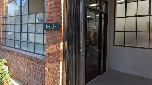 A brick building entrance is picture with a sign reading Oxide.