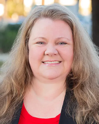 A headshot shows a woman in business attire wearing a navy blazer and red shirt.