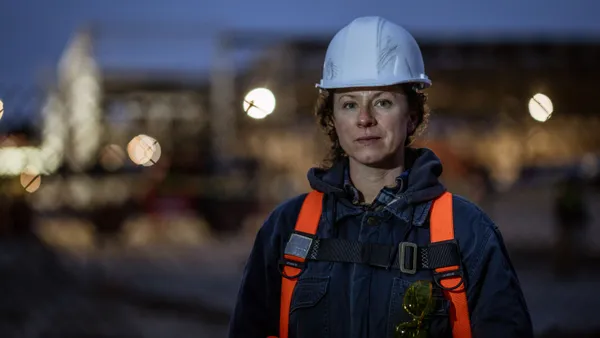 A woman on a construction jobsite at dusk looks into the camera.