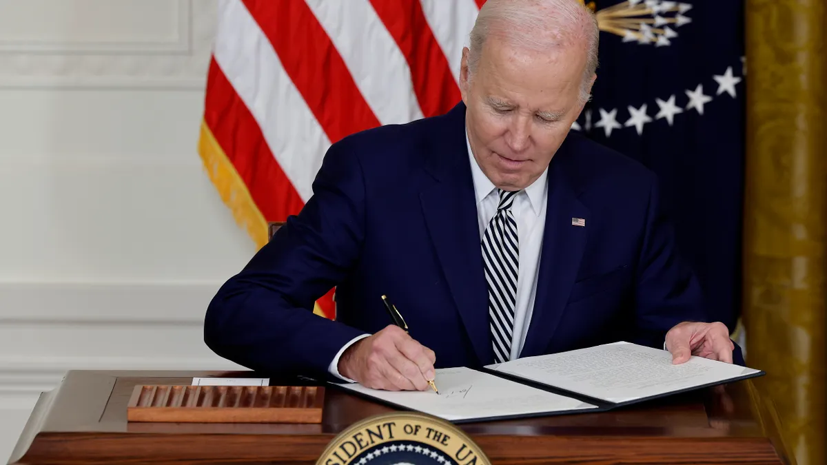 President Joe Biden signs a piece of paper while seated.