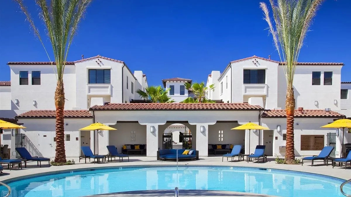 White apartment building with palm trees and a pool in the foreground.