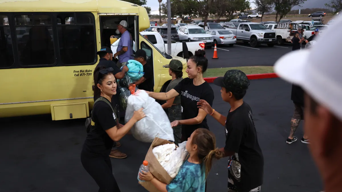 Several volunteers pull white plastic bags of supplies out of a yellow bus.