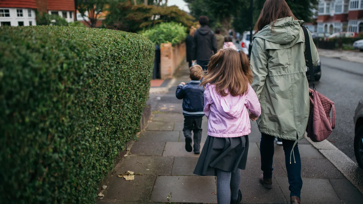 school children and adults walk on a sidewalk