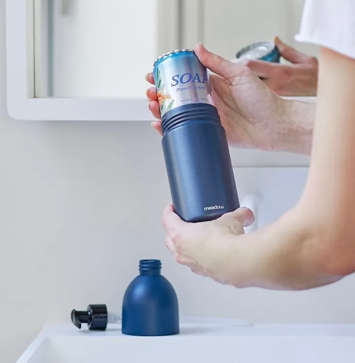 A person inserts a metal can refill into a soap dispensing system.